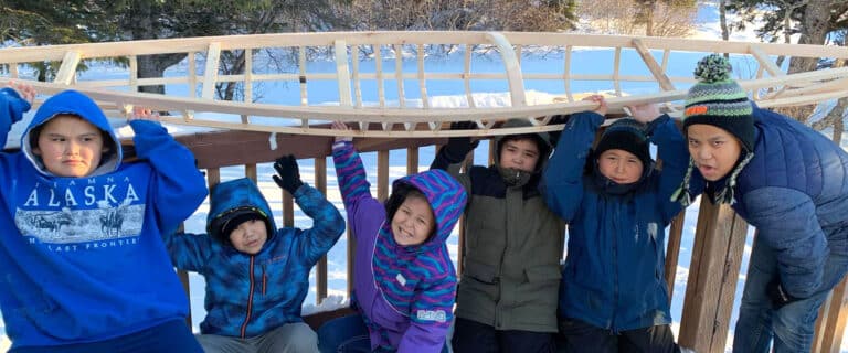 Kids holding a partially built wooden kayak