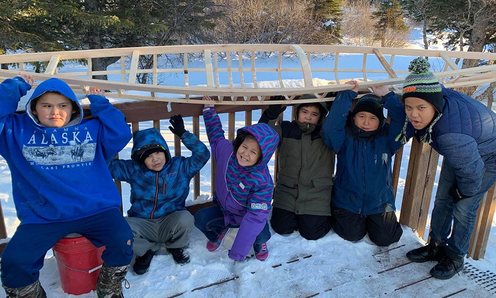 Kids holding a partially built wooden kayak