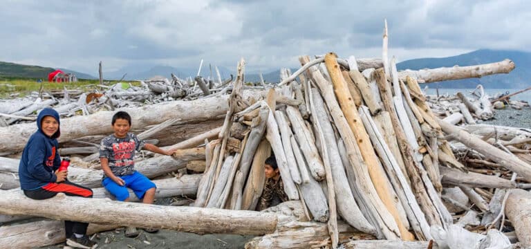 Three kids building a driftwood shelter