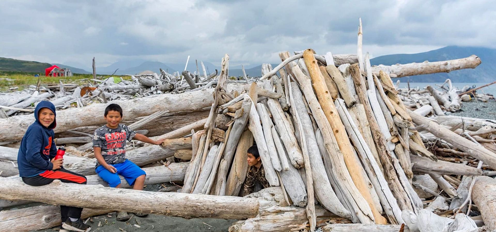 Three kids building a driftwood shelter